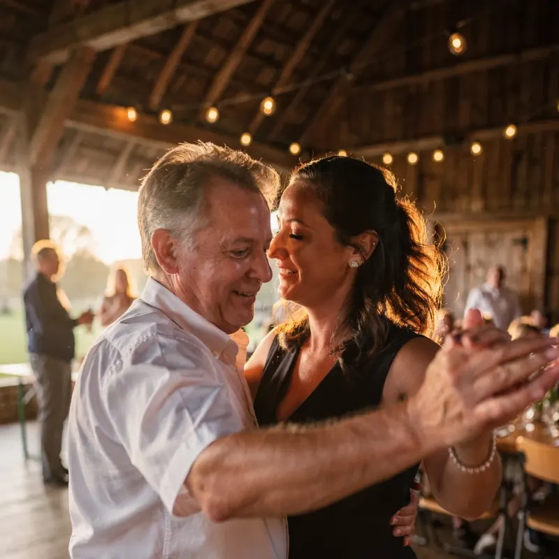 Een stel danst in het avondlicht in een houten schuur tijdens een bruiloft