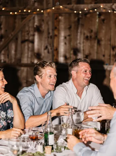 Gasten lachen samen aan een gedekte tafel in een schuur