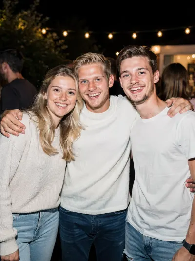 Drie vrienden arm in arm in de tuin, 's avonds onder lichtslingers